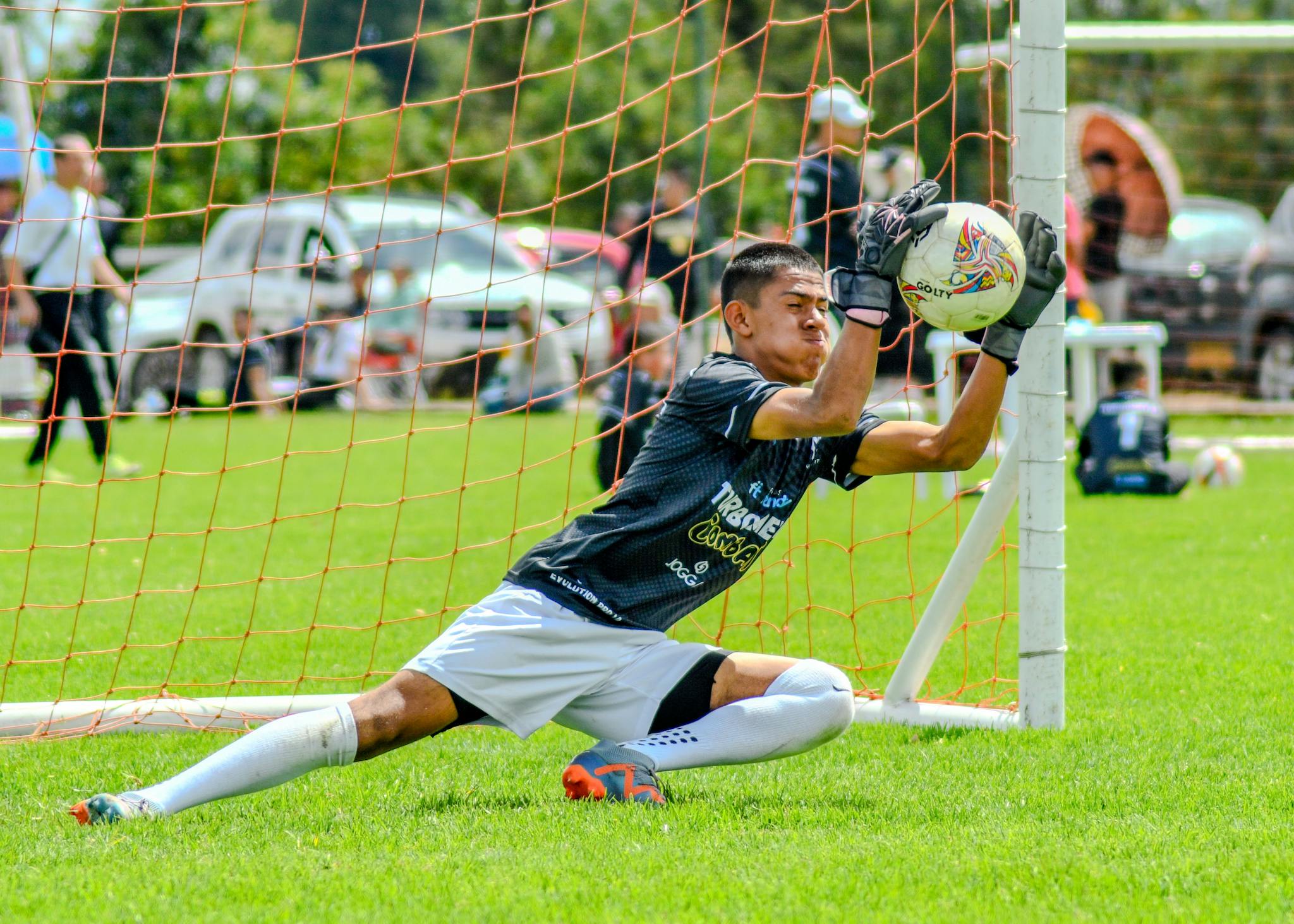 Dynamic action shot of a young goalkeeper catching a soccer ball during a match outdoors.