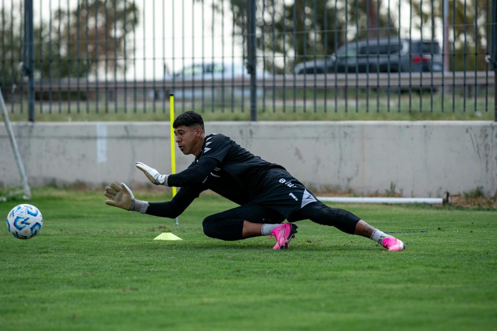 Goalkeeper practicing on a green grass field, focused on saving a soccer ball.